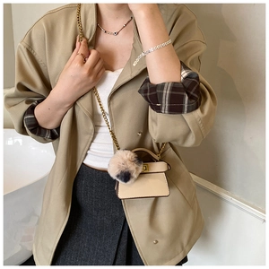 Close-up of a mini cream leather bag with a gold chain strap and a fluffy pompom detail