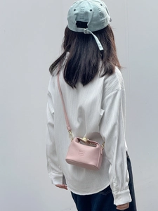 Model wearing a small light pink pebble leather crossbody bag with a square buckle