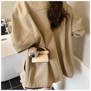 Detail of beige mini crossbody bag with gold buckle and bicolor pompom charm