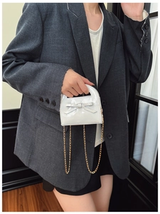 Détail du mini sac blanc en cuir verni avec nœud et chaîne dorée sur mannequin