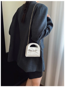 Détail d'un mini sac en cuir verni brillant avec nœud décoratif et chaîne dorée