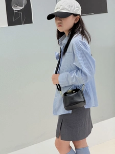 Detail of black pebbled leather mini bag with gold hardware worn by model on shoulder