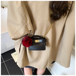 Close-up of black mini chain bag with gold buckle and dark red faux fur ball charm
