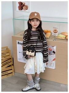 Enfant avec tenue stylée et mini sac à main motif ours dans une boulangerie chaleureuse