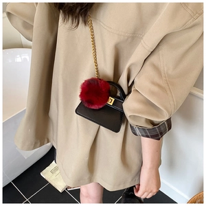 Close-up of a mini black PU leather bag with golden chain strap and a large red pompom
