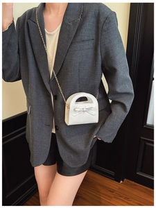 Détail d'un sac à bandoulière en cuir verni blanc pour fille avec nœud et chaîne dorée