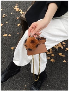 Mini brown leather handbag detail featuring leopard faux fur pom-pom and gold chain strap