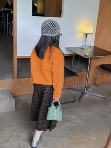 Detail of a child in orange sweater and plaid skirt with mini light green shirt-shaped handbag
