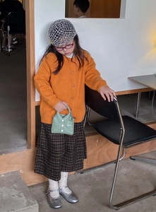 Close-up of girl wearing orange knit cardigan and green shirt-shaped handbag with details