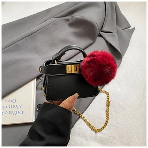 Mini black handbag featuring a large red fur pompom detail and elegant gold chain strap