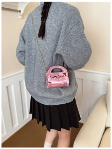 Détail du mini sac en cuir verni rose avec décoration de nœud et bandoulière dorée