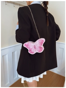 Fillette portant un sac papillon rose avec chaîne dorée sur un blazer noir chic