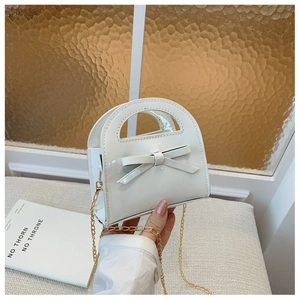 Gros plan du mini sac blanc en cuir verni avec nœud 3D et bandoulière chaîne dorée