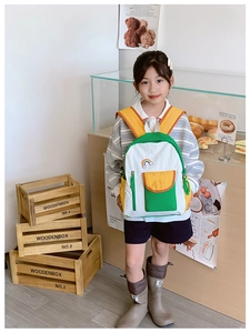 Asian child wearing a tri-color canvas backpack with rainbow patch in a cozy room