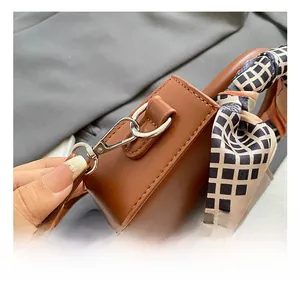 Dettaglio del gancio metallico argento e del manico con foulard di seta sulla borsa marrone