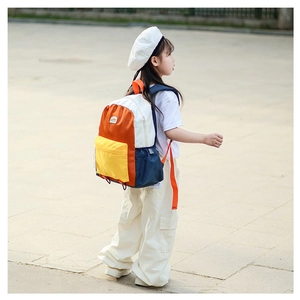 Outdoor view of kids' color-block backpack showing orange straps and side pocket details