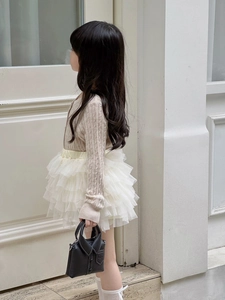 Detail of child wearing beige knit cardigan and white tutu skirt with black mini bag