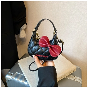 Détail d'un mini sac à main matelassé noir avec un grand nœud rouge et lettrage brodé