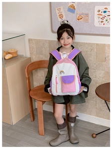 Child wearing a stylish color-block rainbow backpack in a warm cafe setting