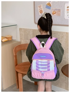 Detail of a pink and purple color-block kids' backpack worn by a girl in a cafe
