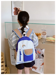 Kid's blue and white rainbow backpack shown on a child model in a cozy bakery setting