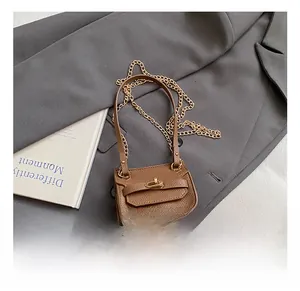 Détail du mini sac bandoulière en cuir marron avec fermoir doré sur un blazer gris