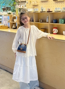Mini girl crossbody bag in blue denim and brown leather held against a white lace dress
