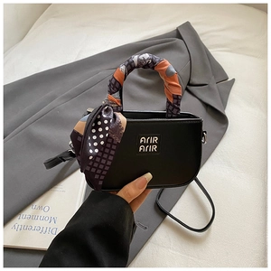 Dettaglio di una mini borsa nera con foulard in seta floreale avvolto intorno al manico