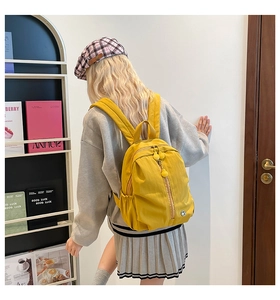 Side view of a bright yellow large-capacity backpack worn by a model in a library setting