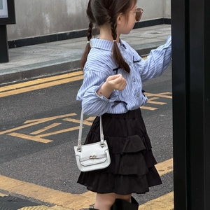 Détail d'un mini sac argenté métallisé assorti à une chemise rayée bleue et jupe