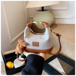 Close-up of small beige canvas handbag with leather logo detail and cute brown plush bear charm