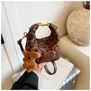 Detail of leopard print plush handbag featuring leather trim and a cute brown bear charm