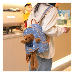 Detail of blue denim backpack with plush bear decoration and floral gold zippers
