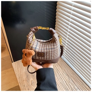 Detail of vintage plaid girl's handbag featuring brown leather base and cute plush bear charm
