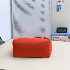 Gros plan sur le sac bandoulière en toile orange vif avec petite étiquette tissée noire