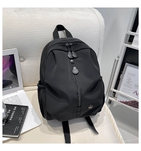 Detail of minimalist black nylon backpack featuring large front pocket and metal logo badge