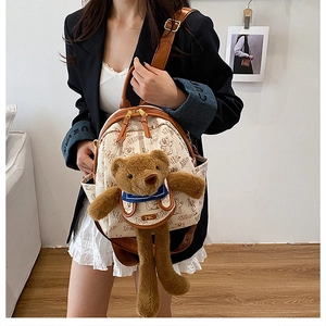 Close-up of a mini cream backpack with a brown plush bear and navy bow on the front