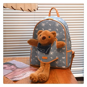 Detail of blue denim backpack featuring a cute plush bear and orange leather accents