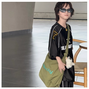 Détail d'un sac bandoulière en toile vert olive avec broderie Lucky et peluche décorative