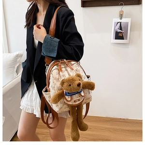 Close-up of a cream PU leather backpack with a 3D plush bear and brand name metal plate