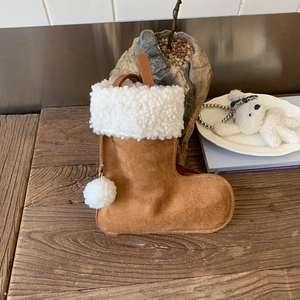Botte de Noël en daim marron avec bordure en polaire blanche et pompons sur table en bois