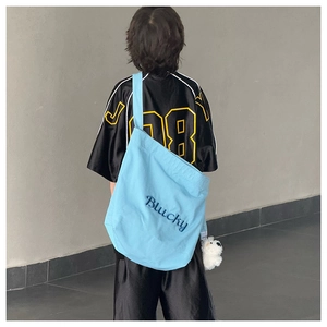 Détail du sac bandoulière en toile bleu clair avec broderie Blucky et ourson peluche
