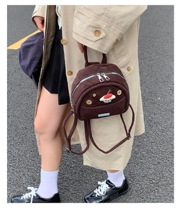 Outdoor lifestyle shot of small dark brown suede backpack with cute plush doll accessory