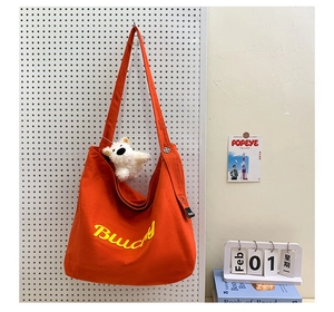 Détail d'un sac cabas en toile orange vif avec broderie jaune et breloque en peluche