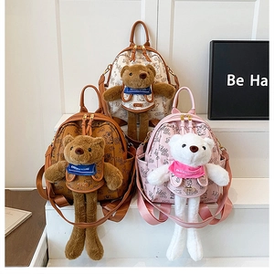 Three mini backpacks with teddy bear charm and monogram pattern in ivory, brown, and pink