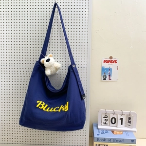 Détail du sac en toile bleu foncé avec broderie Blucky et pendentif ours en peluche