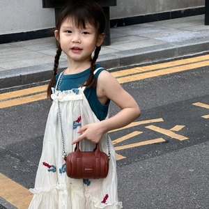 Close-up of brown textured leather cylinder mini bag with silver chain on a young girl