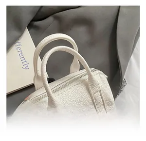 Close-up of white pebble leather mini cylinder bag with dual handles and metal chain