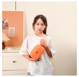 Bright orange mini crossbody chest bag shown on child model in cozy indoor setting
