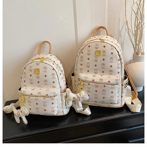 Detailed view of cream backpacks with brown bear monogram and dog charms in two sizes